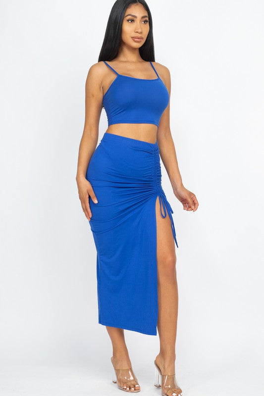 Shop the Jenny Two-Piece Skirt Set, featuring a cropped square-neck top and high-waisted midi skirt with adjustable ruching and a statement side slit.