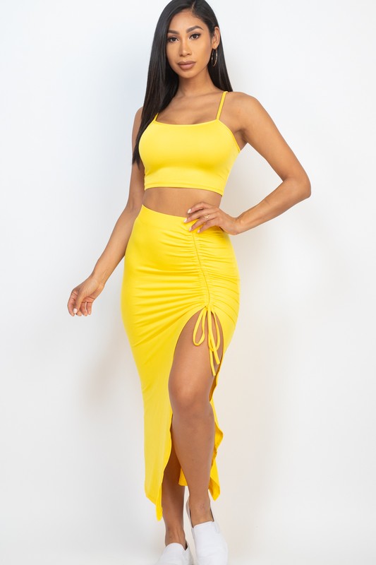 Shop the Jenny Two-Piece Skirt Set, featuring a cropped square-neck top and high-waisted midi skirt with adjustable ruching and a statement side slit.