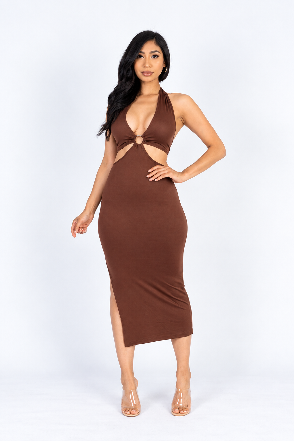 A woman modeling a brown halter midi dress with a cutout at the waist and a side slit, paired with clear high-heeled sandals, against a plain white studio background.